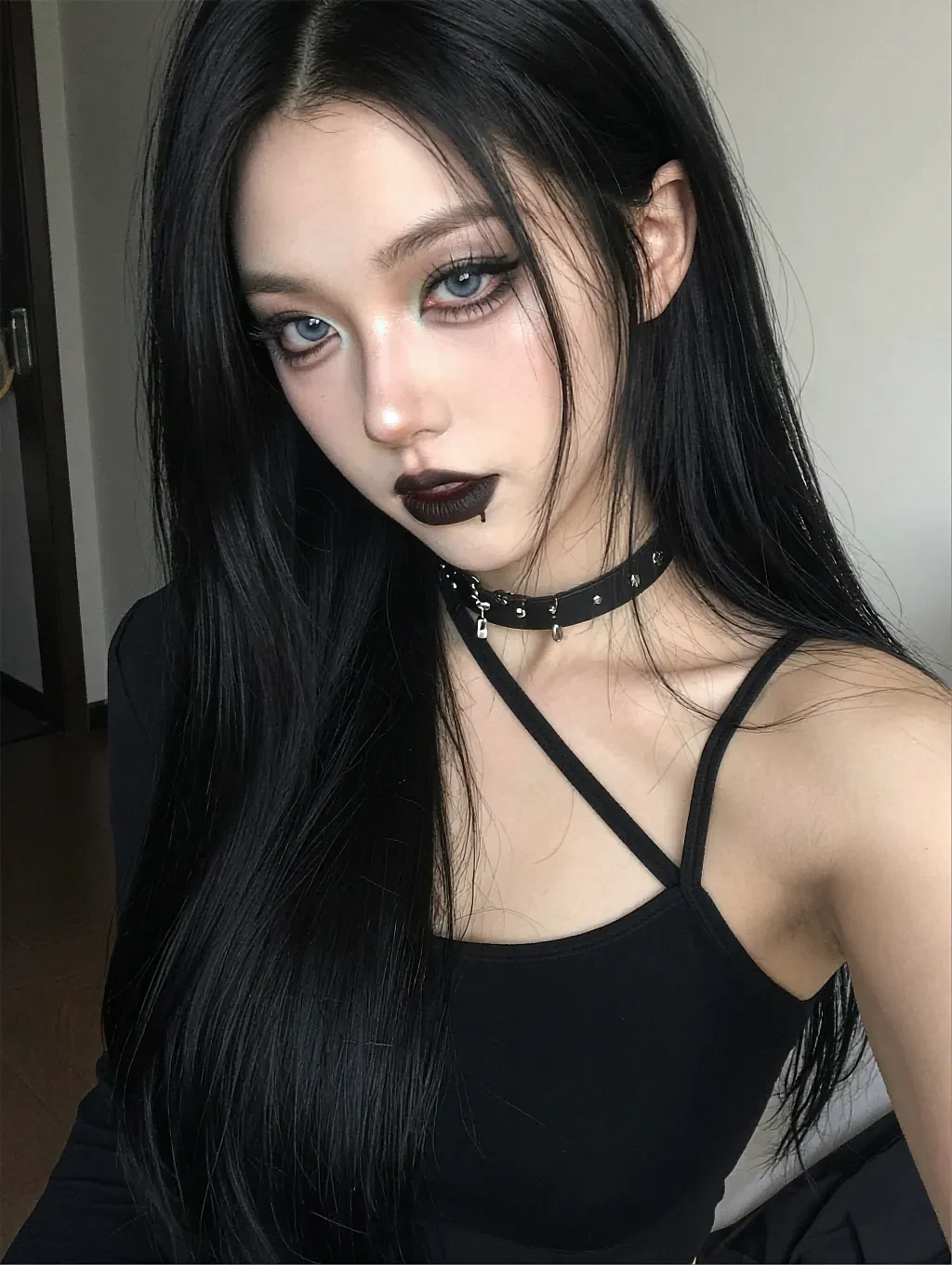 Fictional AI character with black hair and dark lipstick in a strappy black top, photographed in daylight indoors